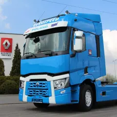 Błękitny ciągnik siodłowy Renault Trucks, jeden z nowoczesnych renault modele, stoi przed budynkiem z logo marki.