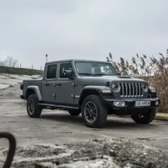 Szary Jeep Gladiator na betonowym podłożu, z suchymi trawami w tle.