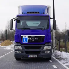 Niebieska ciężarówka z literą L na masce, gotowa do drogi. Kierowca ciężarówek wyrusza w trasę.