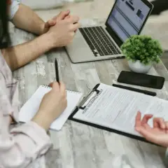 Osoby przy stole omawiają dokument "Home Insurance Policy". Kobieta notuje, mężczyzna patrzy na laptopa. Może to być związane z wefox wypowiedzenie oc.