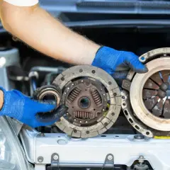 Mechanik w niebieskich rękawiczkach trzyma zużyte części sprzęgła. Zastanawiasz się nad wymiana sprzęgła koszt?