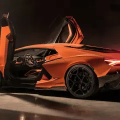 Pomarańczowy Lamborghini Revuelto z otwartymi drzwiami typu nożycowego, z widocznym wnętrzem i sportowymi felgami.
