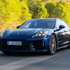 Niebieski Porsche Panamera 2024 pędzi po krętej drodze wśród zielonych wzgórz.