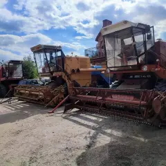 Dwa kombajny Bizon stoją obok siebie na placu. Jeden jest czerwony, drugi żółty.