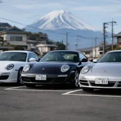 Trzy Porsche 911: białe, czarne i srebrne, zaparkowane na tle ośnieżonego Fuji.