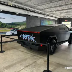 Czarny Tesla Cybertruck z neonowym napisem "CYBERTRUCK" na tyle. W tle reklama "Electric All-Wheel Drive". Cena tego futurystycznego pojazdu budzi zainteresowanie.