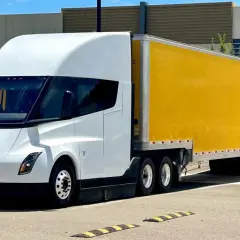 Biały Tesla Semi z żółtą naczepą DHL stoi na parkingu.
