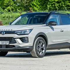 Jasnoszary SsangYong Korando z czarnym dachem stoi na drodze gruntowej, otoczony zielenią.