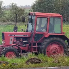 Czerwony traktor Belarus 820 pracuje na polu, za nim widać las.