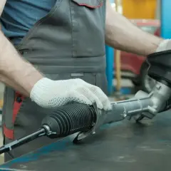 Mechanik w białych rękawiczkach trzyma element układu kierowniczego samochodu.