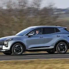 Srebrny SUV Kia Sportage, jeden z najnowszych modeli, jedzie po drodze.