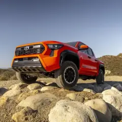 Pomarańczowa Toyota Tacoma pokonuje skalisty teren, gotowa na każdą przygodę.