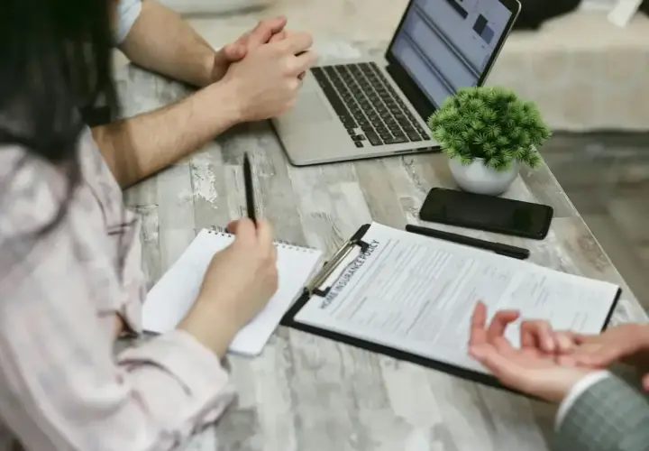 Osoby przy stole omawiają dokument "Home Insurance Policy". Kobieta notuje, mężczyzna patrzy na laptopa. Może to być związane z wefox wypowiedzenie oc.
