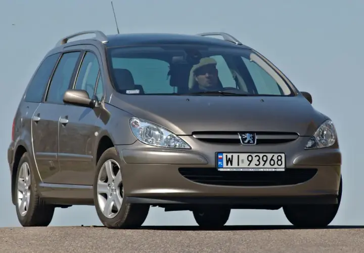 Brązowe kombi Peugeot 307 z kierowcą w jasnej czapce na tle błękitnego nieba.