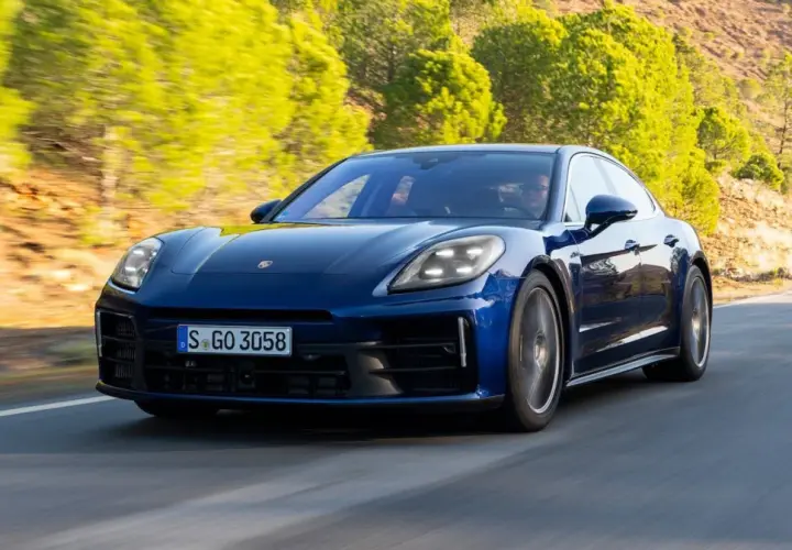 Niebieski Porsche Panamera 2024 pędzi po krętej drodze wśród zielonych wzgórz.