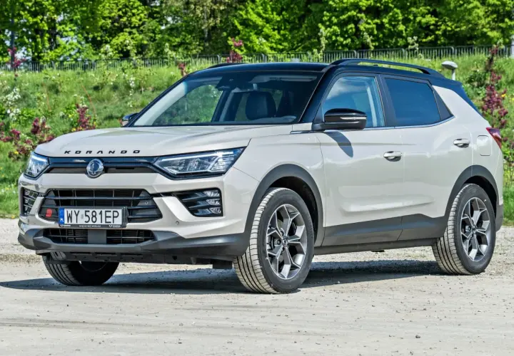 Jasnoszary SsangYong Korando z czarnym dachem stoi na drodze gruntowej, otoczony zielenią.