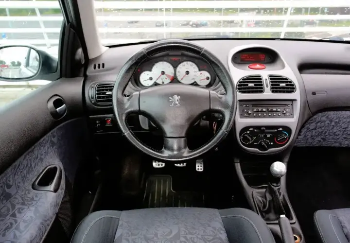 Wnętrze Peugeota 206 1.4 benzyna. Widok na deskę rozdzielczą, kierownicę z logo lwa, radio i dźwignię zmiany biegów.