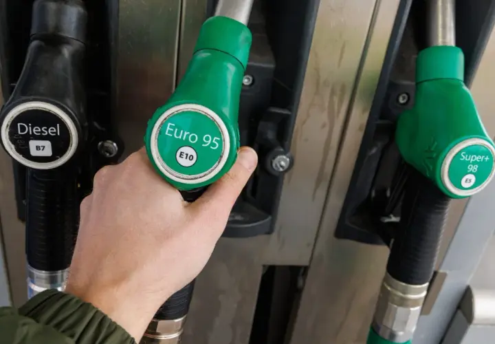 Ręka chwyta zieloną dyszę z napisem "Euro 95 E10" przy dystrybutorze paliwa. Idealne dla Kia Ceed 1.4 benzyna.