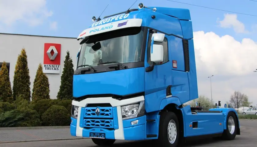 Błękitny ciągnik siodłowy Renault Trucks, jeden z nowoczesnych renault modele, stoi przed budynkiem z logo marki.