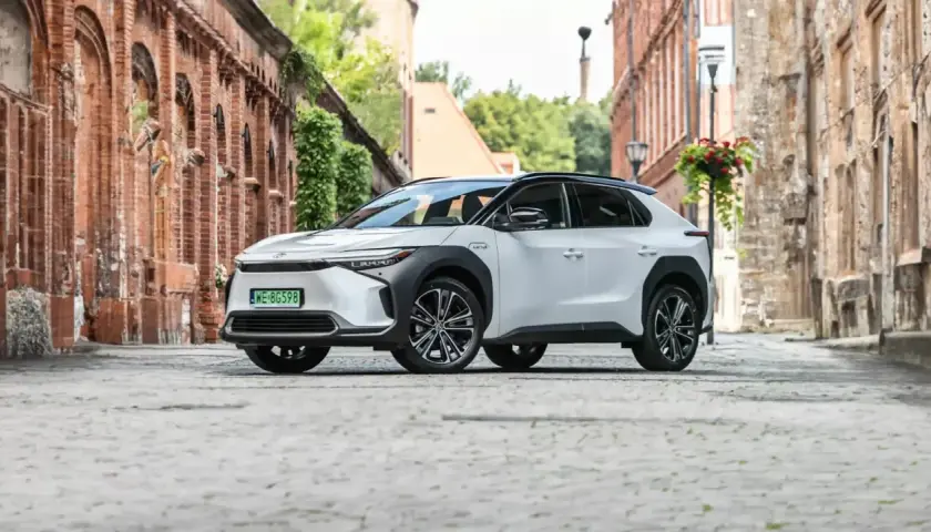 Biały Toyota bz4x na brukowanej uliczce starego miasta, otoczony ceglanymi budynkami i zielenią.