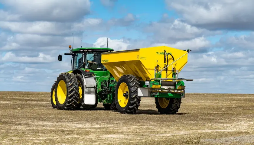 Zielony John Deere 7810 z żółtym rozsiewaczem Landaco T130 na polu.