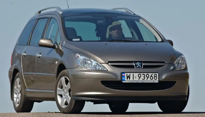 Brązowe kombi Peugeot 307 z kierowcą w jasnej czapce na tle błękitnego nieba.