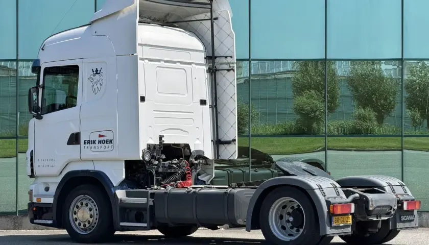 Biała Scania R420 z logo "Erik Hoek Transport" stoi przed nowoczesnym budynkiem z zielonymi oknami.