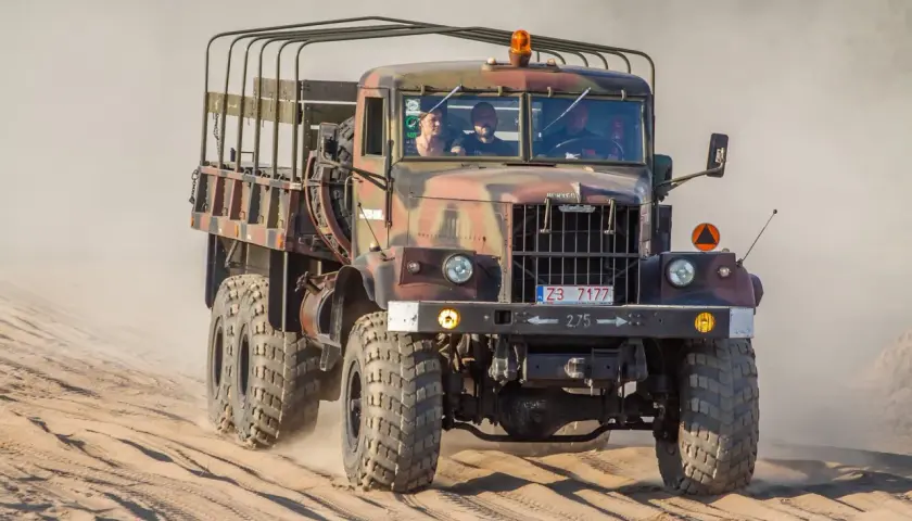 Kraz 255 z załogą przemierza piaszczysty teren, wzbijając tumany kurzu.