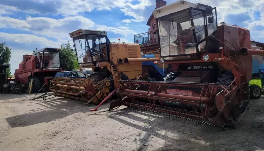 Dwa kombajny Bizon stoją obok siebie na placu. Jeden jest czerwony, drugi żółty.