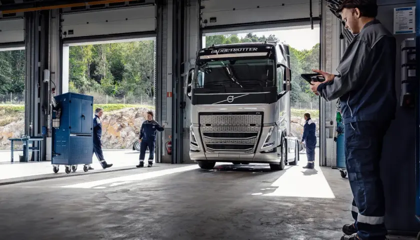 Mechanicy w serwisie obsługują nowoczesną ciężarówkę Volvo FH4. Jeden z nich sprawdza coś na tablecie.