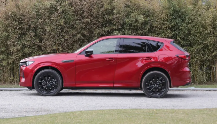 Czerwona Mazda CX-60 3.3 diesel z czarnymi felgami stoi na żwirowej drodze, za nią gęsty żywopłot.