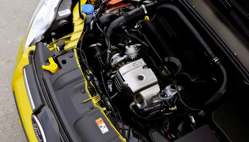 Silnik 1.0 Ecoboost w żółtym Fordzie. Widoczne elementy układu dolotowego, turbosprężarki i osłony silnika.