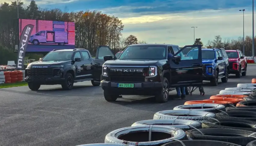 Kolekcja nowoczesnych pickupów Maxus, w tym czarny model z otwartymi drzwiami, ustawiona na torze wyścigowym.