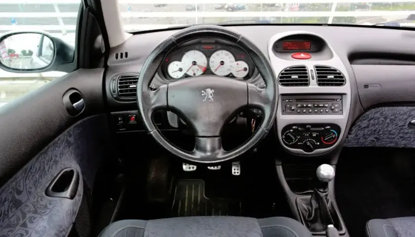 Wnętrze Peugeota 206 1.4 benzyna. Widok na deskę rozdzielczą, kierownicę z logo lwa, radio i dźwignię zmiany biegów.