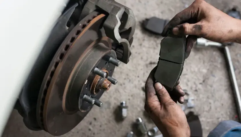 Mechanik pokazuje zużyte klocki hamulcowe przed wymianą.