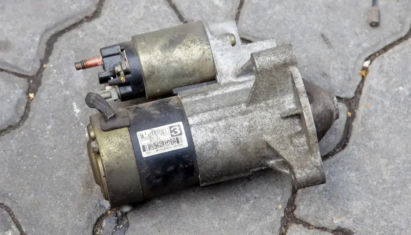 Dwa używane rozruszniki w aucie, jeden na drugim, leżą na betonowej nawierzchni.