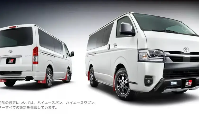 Dwa białe vany Toyota Hiace z pakietem GR Parts, jeden z tyłu, drugi z przodu, z czerwonymi błotnikami.