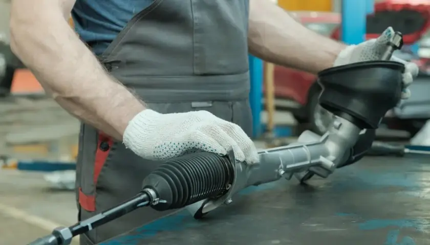 Mechanik w białych rękawiczkach trzyma element układu kierowniczego samochodu.