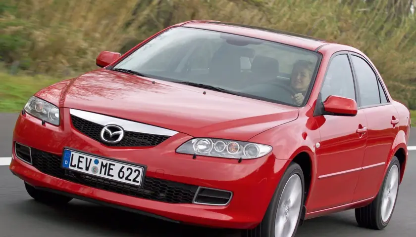 Czerwona Mazda 6 2.0 benzyna w ruchu, za kierownicą uśmiechnięta kobieta.