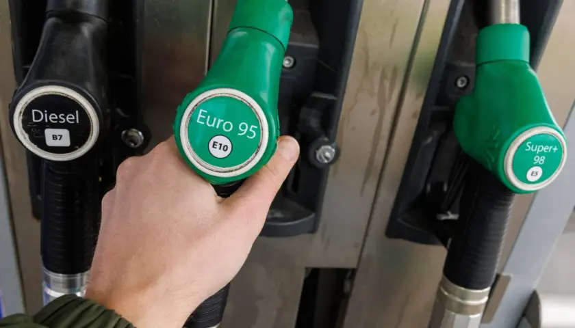 Ręka chwyta zieloną dyszę z napisem "Euro 95 E10" przy dystrybutorze paliwa. Idealne dla Kia Ceed 1.4 benzyna.