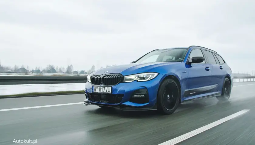 Niebieskie BMW 330e na mokrej drodze, z widocznymi kroplami deszczu na karoserii.