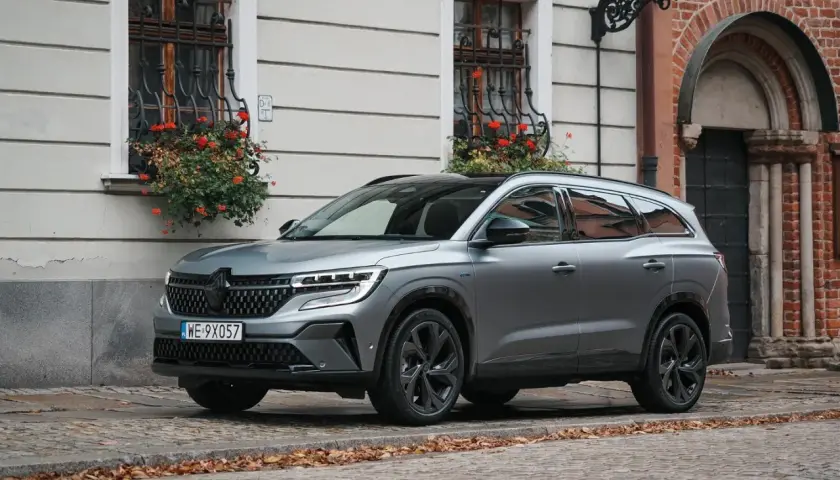 Nowy Renault Espace 2024 w szarym kolorze na brukowanej uliczce, z kwiatami w oknach.