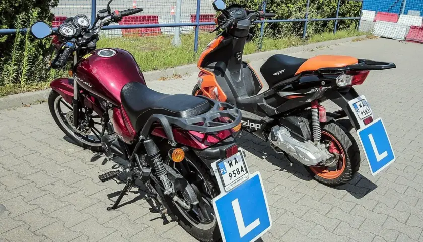 Dwa pojazdy z literą "L" na niebieskiej tablicy, sugerujące naukę jazdy.