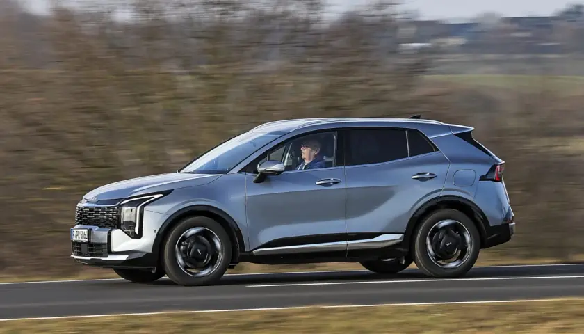 Srebrny SUV Kia Sportage, jeden z najnowszych modeli, jedzie po drodze.