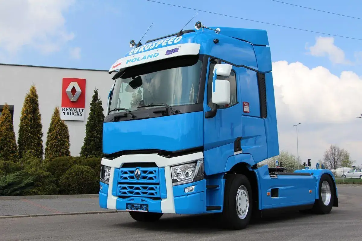Błękitny ciągnik siodłowy Renault Trucks, jeden z nowoczesnych renault modele, stoi przed budynkiem z logo marki.