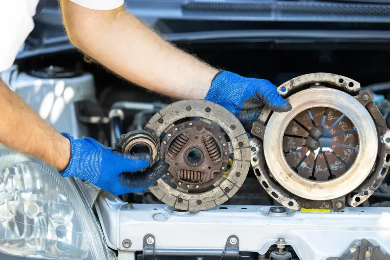 Mechanik w niebieskich rękawiczkach trzyma zużyte części sprzęgła. Zastanawiasz się nad wymiana sprzęgła koszt?