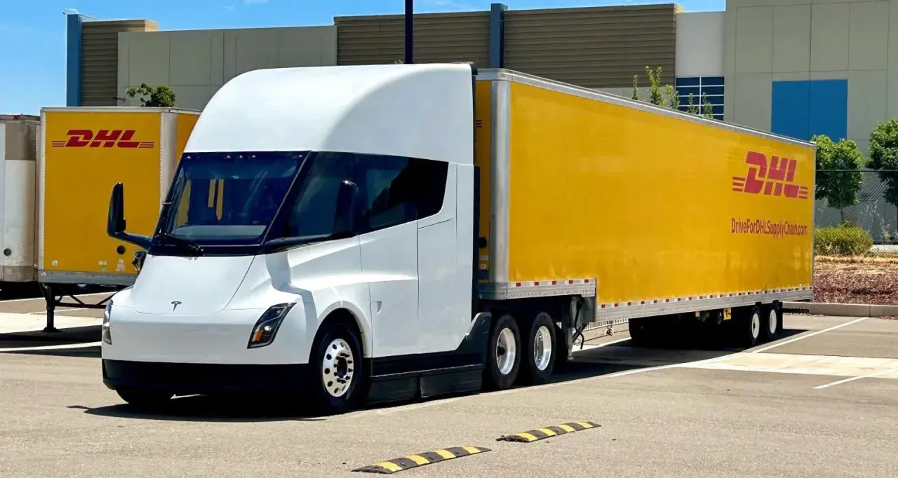 Biały Tesla Semi z żółtą naczepą DHL stoi na parkingu.