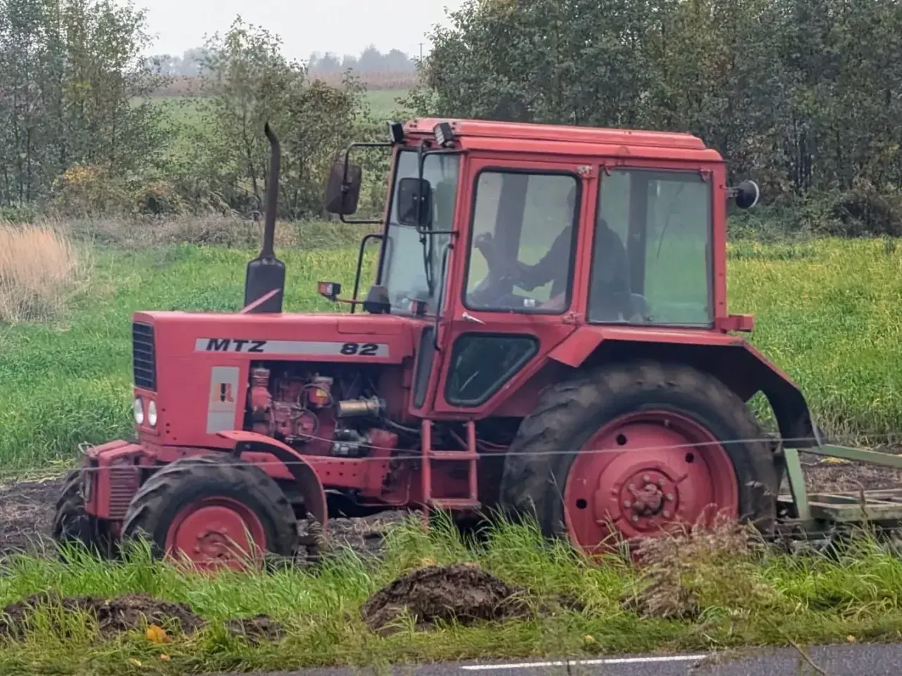 Czerwony traktor Belarus 820 pracuje na polu, za nim widać las.