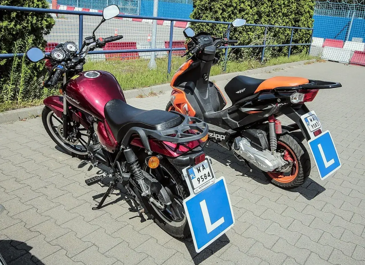 Dwa pojazdy z literą "L" na niebieskiej tablicy, sugerujące naukę jazdy.