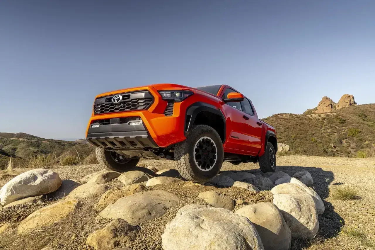 Pomarańczowa Toyota Tacoma pokonuje skalisty teren, gotowa na każdą przygodę.